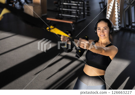 Young beautiful Asian woman doing fitness exercises on the TRX machine in the gym. 126663227