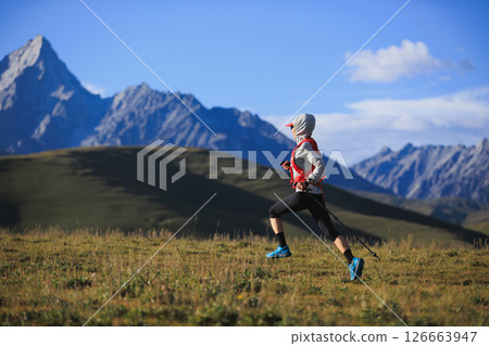 Fitness woman trail runner running in grassland with snow capped mountains in the background 126663947