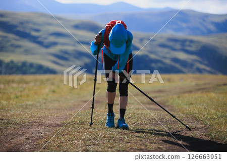 Tired woman trail runner running in grassland with snow capped mountains in the background Tired woman trail runner running in grassland with snow capped mountains in the background 126663951