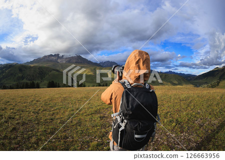 Woman backpacker hiking on high altitude mountains taking picture of the snow capped mountain in the distance Woman backpacker hiking on high altitude mountains taking picture of the snow capped mountain in the distance 126663956