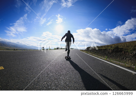 Skateboarder skateboarding on the mountain road Skateboarder skateboarding on the mountain road 126663999