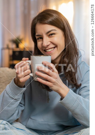 Happy young woman smelling drinking cup of hot coffee, taking a break, relaxing on sofa at home Happy young woman smelling drinking cup of hot coffee, taking a break, relaxing on sofa at home 126664178