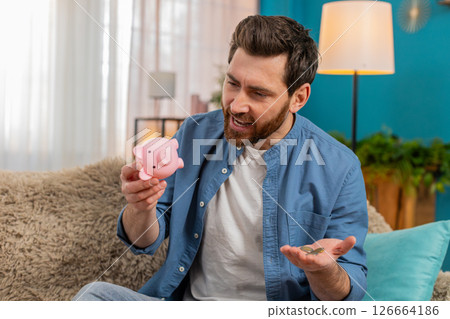 Man shaking piggy bank, counting collected coins, saving money, checking personal finances at home Man shaking piggy bank, counting collected coins, saving money, checking personal finances at home 126664186