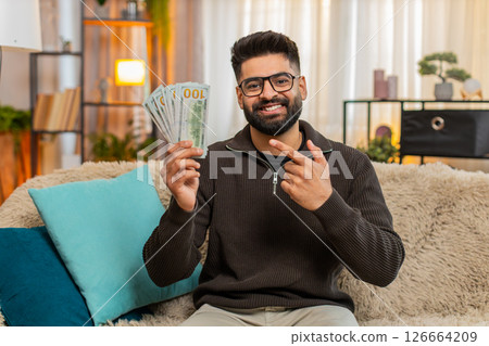 Indian man happily counting cash money on sofa at home, celebrating income or lottery jackpot Indian man happily counting cash money on sofa at home, celebrating income or lottery jackpot 126664209