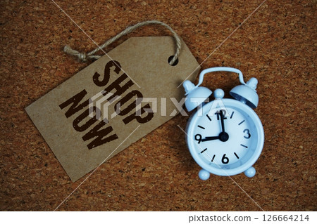 Shop Now text on price tag with alarm clock on cork board background 126664214