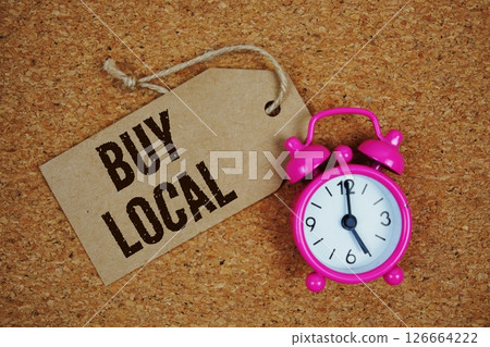 Buy Local text on price tag with alarm clock on cork board background Buy Local text on price tag with alarm clock on cork board background 126664222