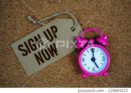 Sign Up Now text on price tag with alarm clock on cork board background Sign Up Now text on price tag with alarm clock on cork board background 126664223