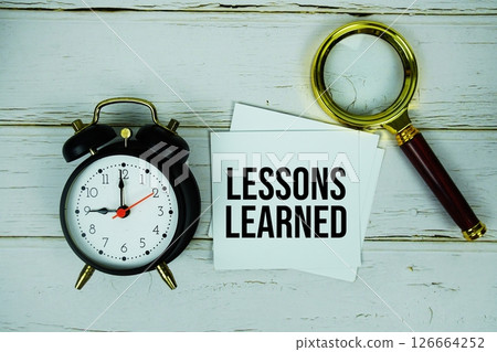 Lessons Learned text message on sticky note with magnifying glass and alarm clock on wooden background Lessons Learned text message on sticky note with magnifying glass and alarm clock on wooden background 126664252