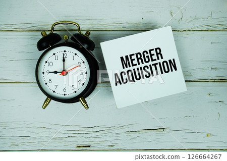 Merger Acquisition text message on sticky note with alarm clock on wooden background 126664267