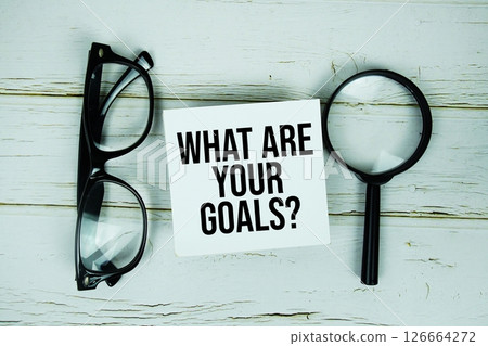 What Are Your Goals? text message on sticky note with magnifying glass and eyeglasses on wooden background 126664272