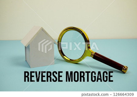 Reverse Mortgage text with White Model House and magnifying glass on blue background Reverse Mortgage text with White Model House and magnifying glass on blue background 126664309