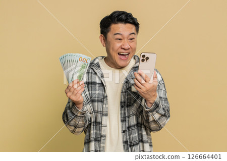 Happy Asian man use smartphone rejoicing game win, receiving money dollar cash, celebrating success Happy Asian man use smartphone rejoicing game win, receiving money dollar cash, celebrating success 126664401