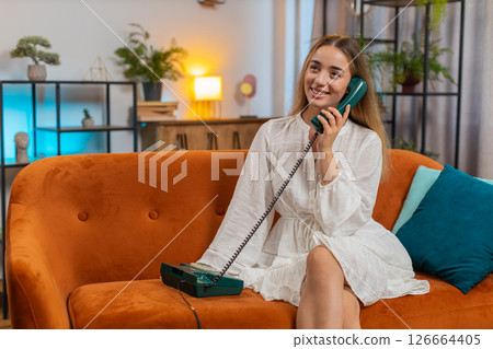 Smiling young woman making wired telephone call conversation with friends sitting on couch at home 126664405