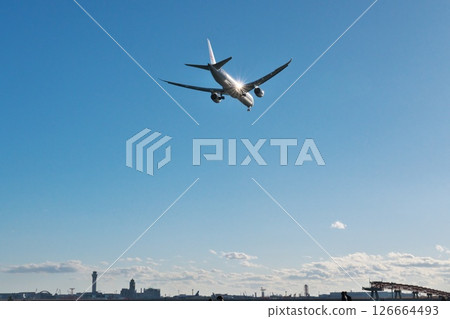 A passenger plane heading to Haneda Airport glitters in the backlight above Jonanjima Seaside Park on a clear winter day A passenger plane heading to Haneda Airport glitters in the backlight above Jonanjima Seaside Park on a clear winter day 126664493