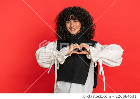 Smiling young woman makes heart gesture demonstrates love sign expresses good feelings and sympathy 126664531