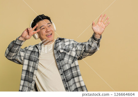 Happy Asian man listening music on headphones and dancing disco fooling around having fun Happy Asian man listening music on headphones and dancing disco fooling around having fun 126664604