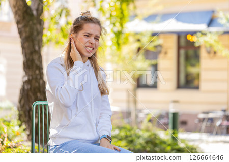 Sick young woman girl teenager suffers from ear pain while sitting on chair in city town street Sick young woman girl teenager suffers from ear pain while sitting on chair in city town street 126664646
