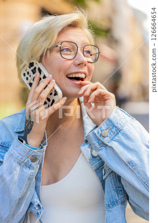 Happy young Caucasian blonde woman with short hair talking gossip on smartphone on city street Happy young Caucasian blonde woman with short hair talking gossip on smartphone on city street 126664654