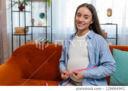 Pregnant woman measuring belly diameter with measure tape awaiting childbirth monitoring body change 126664941
