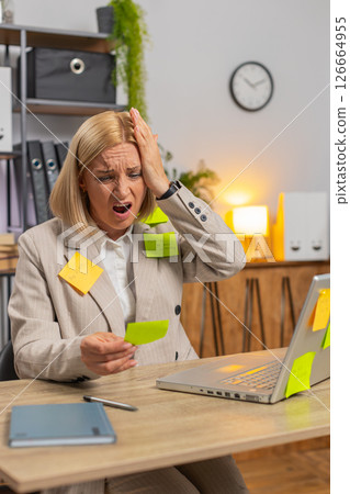 Exhausted Caucasian mature businesswoman with sticky notes and laptop sitting at home office desk 126664955