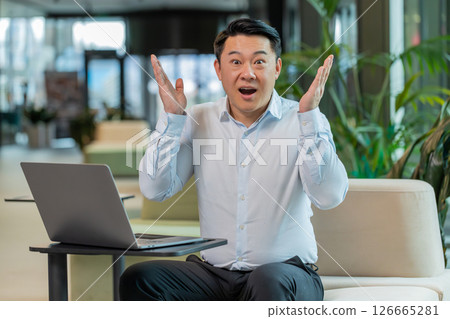 Chinese young businessman in shirt looking at camera shocked by sudden victory in office lobby Chinese young businessman in shirt looking at camera shocked by sudden victory in office lobby 126665281