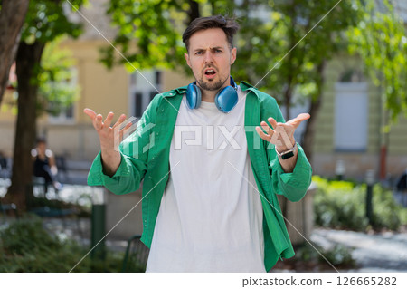 Confused young man feeling embarrassed about ambiguous question having doubts no idea outdoors 126665282