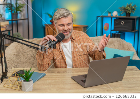 Mature man at home table speaking into microphone during live online stream, responding with energy 126665332