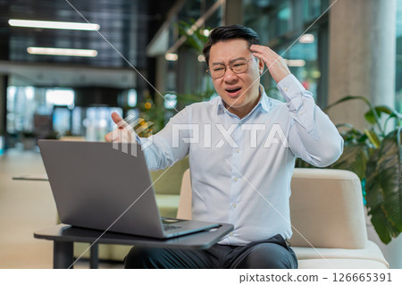 Sad businessman using laptop loses becoming shocked sudden lottery results in modern hotel lobby 126665391