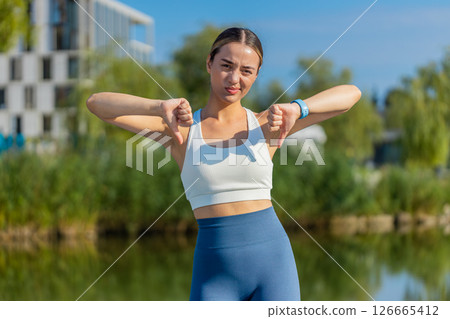 Upset sportswoman showing thumb down sign gesture, expressing disapproval dissatisfied in city park 126665412