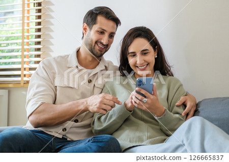 Hispanic Couple sharing social media moments together at home, enjoying digital connection and lifestyle interaction through smartphone 126665837