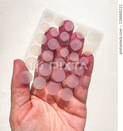 Transparent acne patches on hand shown against a white wall under bright daylight. High quality photo 126668221