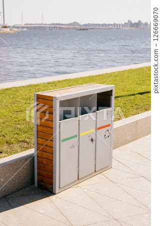 Trash can with three bins sits on a sidewalk next to a body of water. recycling. 126669070