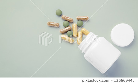 Natural supplement, vitamin spilling out of medical bottle on green background, top view 126669443