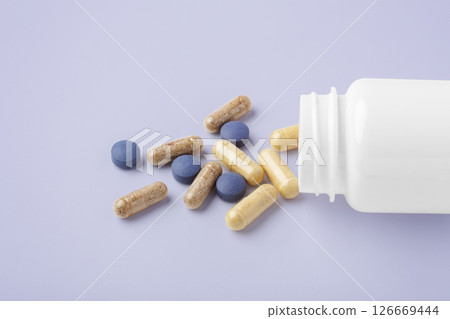Natural supplement, beauty vitamin spilling out of medical bottle on pastel purple background Natural supplement, beauty vitamin spilling out of medical bottle on pastel purple background 126669444