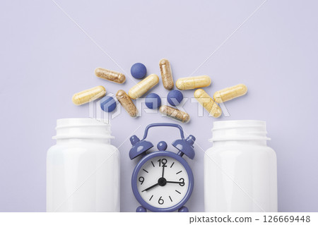 Supplement tablet, beauty vitamin capsule with white bottle and alarm clock on pastel purple background, top view 126669448