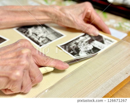 Close-up of an elderly woman peeling black-and-white photos from an album with a knife Close-up of an elderly woman peeling black-and-white photos from an album with a knife 126671267