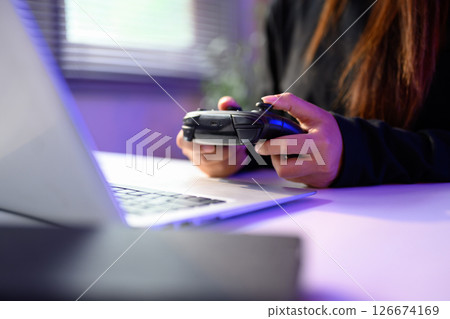 Close up of gamer holding a console controller while playing on a laptop 126674169