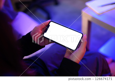 Hands holding smartphone with a blank white screen in a neon lit environment 126674171