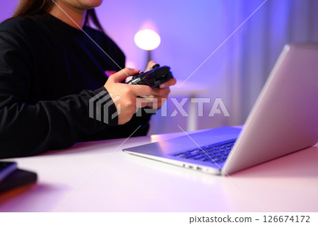 Close up of gamer holding a console controller while playing on a laptop 126674172