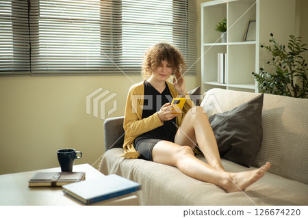 Happy woman in casual wear listens to music on headphones while scrolling her phone 126674220