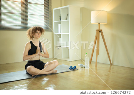 Peaceful young woman practices meditation in a bright home Peaceful young woman practices meditation in a bright home 126674272