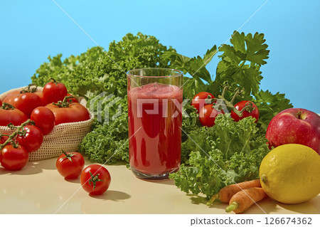 Fresh fruits and vegetables like kale, tomato, and orange laid out on a clean blue tabletop, creating a bold contrast and healthy lifestyle message. A glass of delicious red juice is displayed 126674362