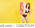 Cheerful Caucasian model in swimsuit hold soft serve cone and donut ring float on vibrant yellow studio backdrop with blank space ideal for lifestyle marketing, tropical travel, or dessert campaigns 126675529