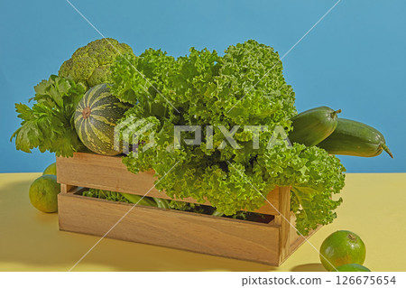 A wooden crate filled with curly kale and leafy greens is styled on a vibrant blue background. The setup combines organic textures with a pop of color for visual contrast. A wooden crate filled with curly kale and leafy greens is styled on a vibrant blue background. The setup combines organic textures with a pop of color for visual contrast. 126675654