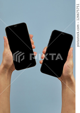 woman holding two smartphones with blank screens on blue background woman holding two smartphones with blank screens on blue background 126675751