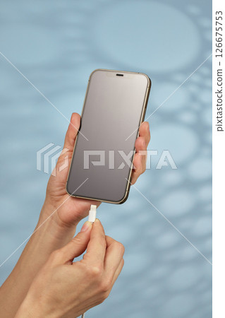 female hand plugging charger cord into smartphone to charge battery on blue background, Wired charging 126675753