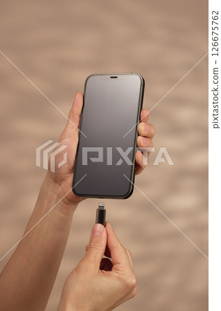 female hand plugging charger cord into smartphone to charge battery on beige background, Wired charging 126675762