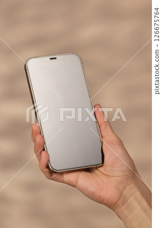 woman holding smartphone with blank screen on beige background, mockup 126675764
