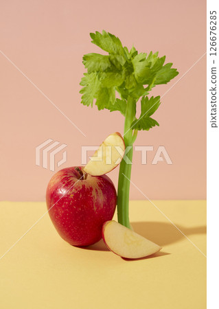 A red apple and celery stalk are artfully arranged on a pastel background. The combination of shadow and minimalist styling creates a creative food concept. A red apple and celery stalk are artfully arranged on a pastel background. The combination of shadow and minimalist styling creates a creative food concept. 126676285