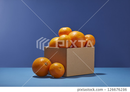 Orange tangerines are placed in a small brown box on a blue background. The vivid contrast makes the citrus fruit pop with freshness and color. Food art with fresh fruit Orange tangerines are placed in a small brown box on a blue background. The vivid contrast makes the citrus fruit pop with freshness and color. Food art with fresh fruit 126676286